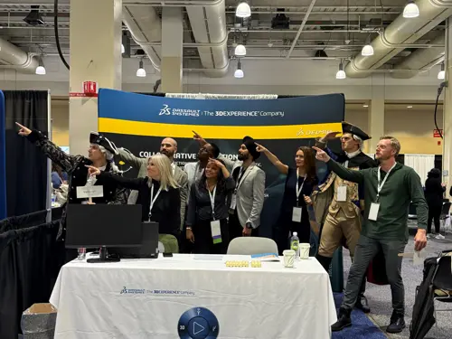 Andea's team, some in historical costumes, pose together at the WIM Summit booth, pointing forward to illustrate solutions for manufacturing efficiency, MES, and APS. A white tablecloth displays the Andea logo and conference branding.