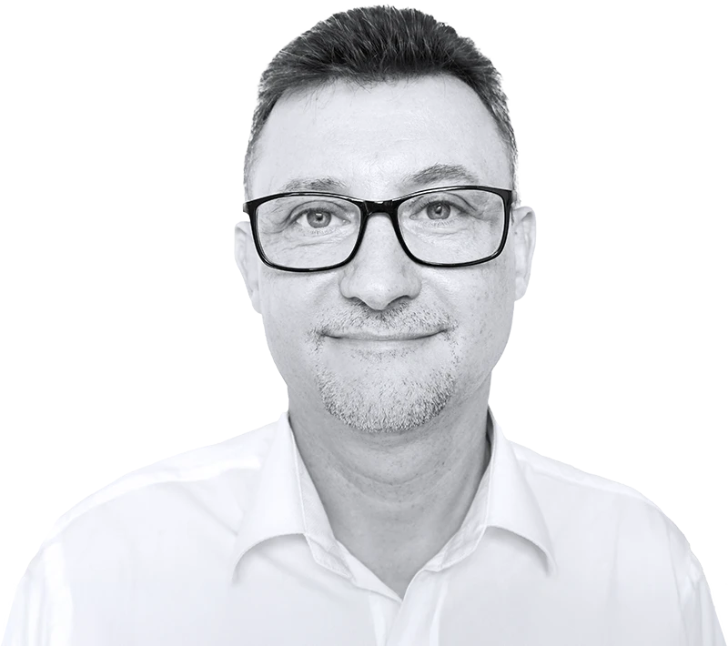 Grzegorz Nowak wears black-rimmed glasses and a white collared shirt. He has short, dark hair and a goatee, with a subtle smile.