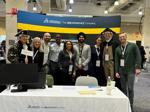 Team at WIM Summit 2023: Andea and Dassault Systèmes representatives pose with a large branded backdrop. One person in historical costume holds a TeamSense sign. Offers MES, APS solutions.