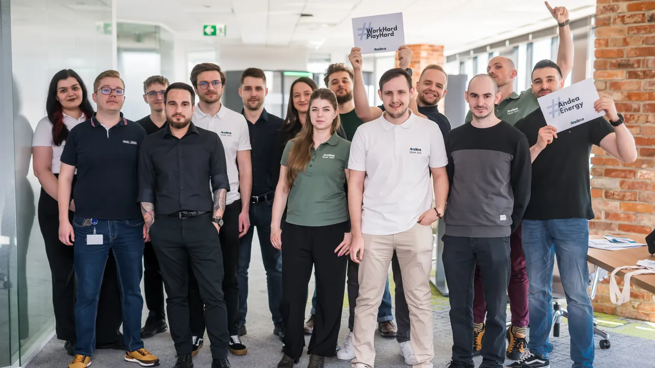 A diverse testing team poses for a photo in a modern office. Two people hold signs saying #WorkHardPlayHard and #Andea Energy.