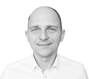 Headshot of Tomasz Gęsiarz, Director of Services at andea.com, in a white collared shirt, smiling at the camera in a black and white professional portrait.