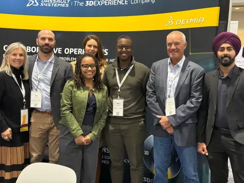 A diverse group of six professionals smile at the camera at the ANDEA DS Summit 2024, posing in front of a branded backdrop featuring Dassault Systèmes and DELMIA.