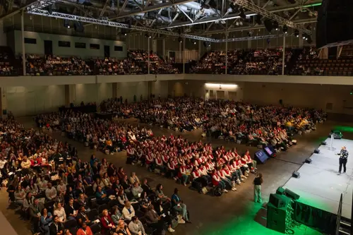 Large audience attending a manufacturing technology summit on Summit Day 1. A speaker presents on a stage to hundreds of seated attendees in a convention hall.